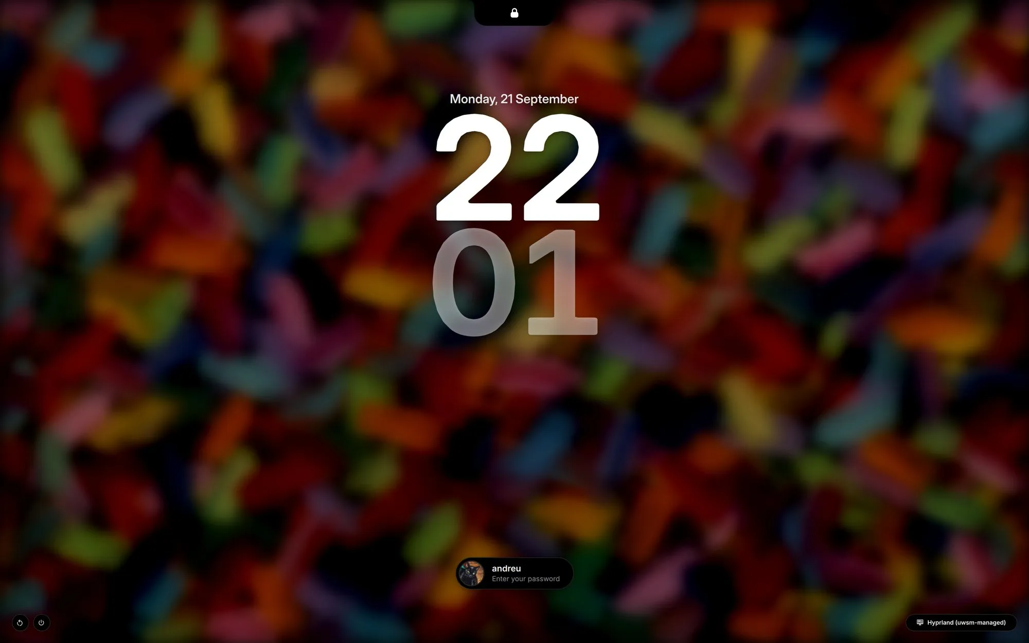 The login screen awake over a blurred, darkened painting of coloured brush strokes: the island with its padlock at the top, the stacked clock, the account pill with andreu and Enter your password, the session name in the bottom-right corner and the power buttons in the bottom-left.
